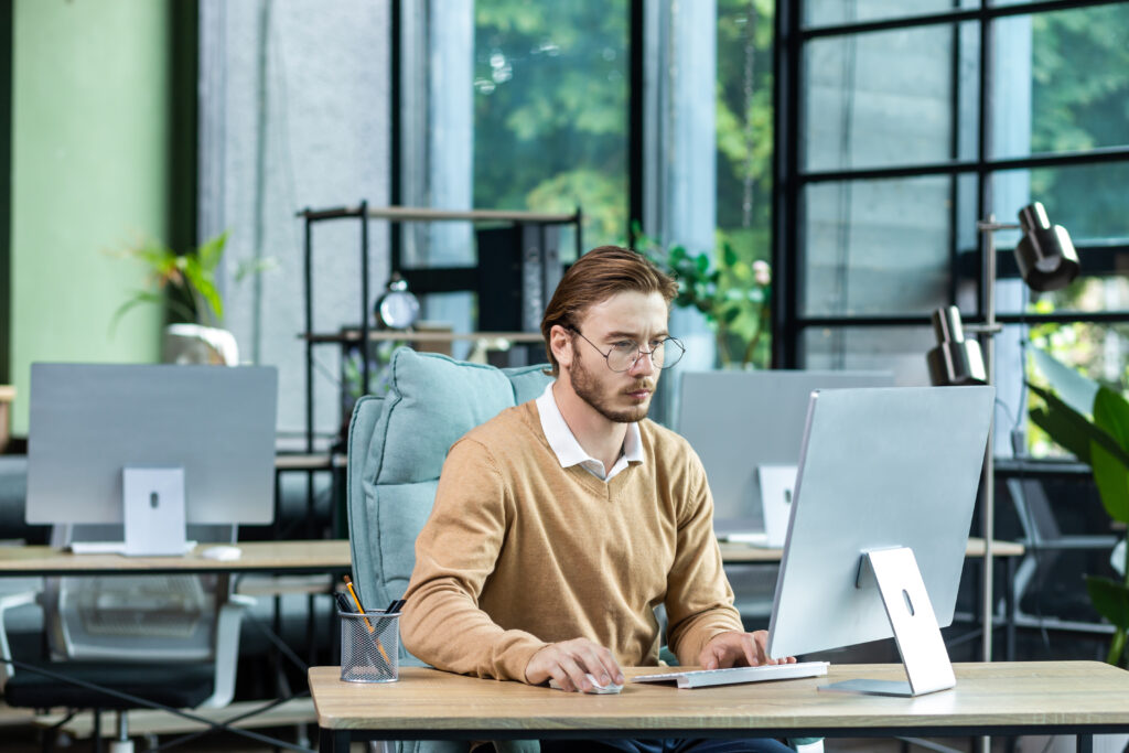 Serious And Scorn Centered Man In The Office At Work With A Computer, Man Typing Thoughtfully On Keyboards, Businessman Young Blond In Sweater Indoors Loft, With Green Colors, Programmer At Work - HERÓI CONTADOR